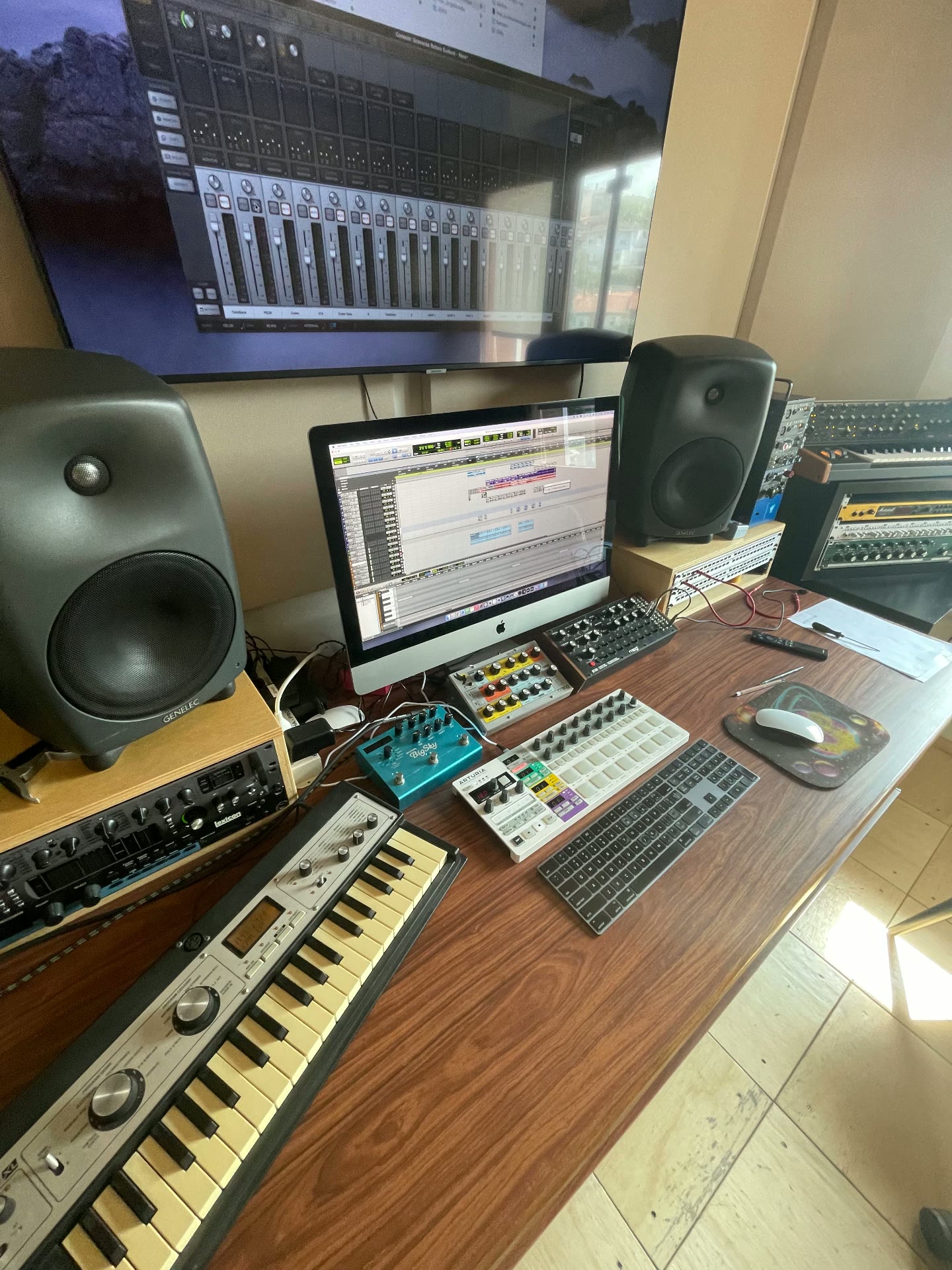 Mesa de trabalho com monitores Genelec, sintetizadores e teclado controlador